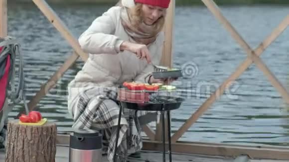 一位穿着保暖衣服的女游客在河岸附近的一座桥上背着背包准备烤蔬菜野餐视频的预览图