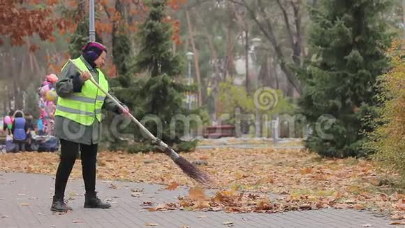 老妇人打扫城市公园停下来休息看着美丽的秋天视频的预览图