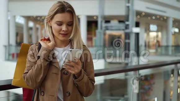 女孩看着手机里的东西站在商场里肩上放着购物袋视频的预览图