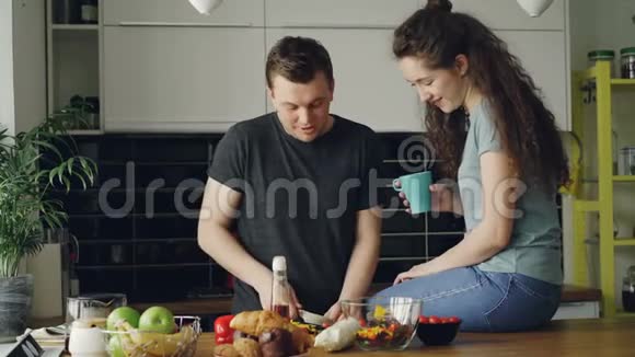 一对快乐的年轻夫妇在家的厨房里切蔬菜吃早餐一边一边一边一边做饭一边愉快地聊天视频的预览图