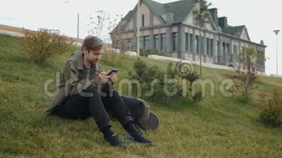 有魅力的年轻人带着笔记本电脑包沿着城市的河流走着打着电话坐在草地上视频的预览图