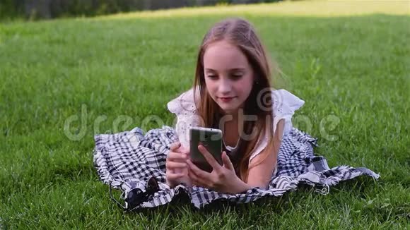 年轻漂亮的女孩用电话躺在公园的草地上视频的预览图
