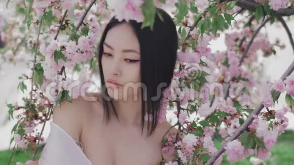 一个美丽的亚洲女孩在户外与春天的花朵树的肖像后台视频的预览图