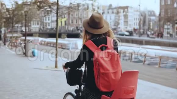 女人骑自行车在拥挤的老街上后视慢动作戴着红色背包的戴着帽子骑自行车的女人视频的预览图