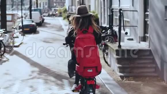 旅游女孩骑自行车在阳光明媚的城市街道向右转骑自行车戴帽子的欧洲女孩后视慢动作视频的预览图