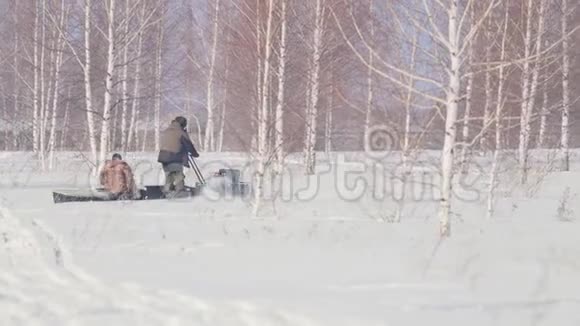 两个人骑着一辆小型雪车在冬天的森林里穿行拖车在树林间移动视频的预览图