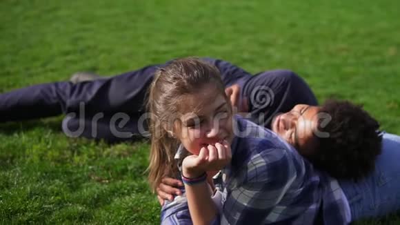 英俊的非洲男人躺在他的白种人女朋友的背上在绿野上说话多民族夫妇视频的预览图