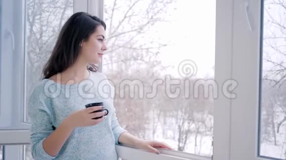 周末愉快可爱的女人站在敞开的窗户边喝热咖啡视频的预览图