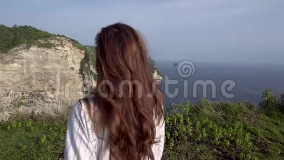 女人举起双手站在海边的悬崖上视频的预览图