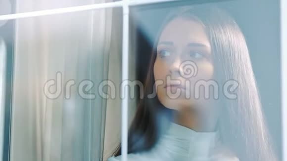 站在窗边独自沉思的悲伤女人视频的预览图