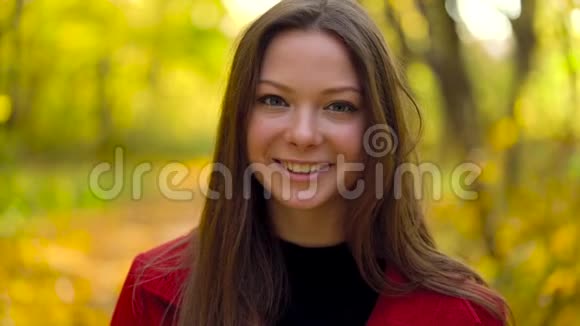 秋天的森林中一个美丽的微笑女孩的肖像前景是一片黄色的枫叶慢动作视频的预览图