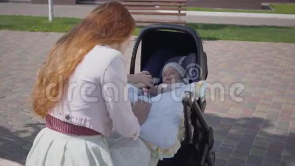 美丽的红发女人和她的孩子在公园里躺在婴儿车里玩这位女士和她一起享受阳光明媚的一天视频的预览图