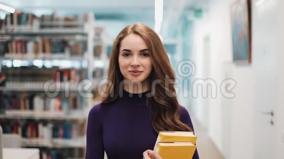 留着长发的女孩直视着摄像机沿着图书馆的书架走着视频的预览图