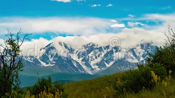 时间流逝云层覆盖着背景中白雪覆盖的山脉前景中灌木在风中摇动视频的预览图