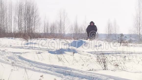 穿着冬季服装的成年男子骑着小雪车在雪地里快速跳跃拖着拖车停下来视频的预览图