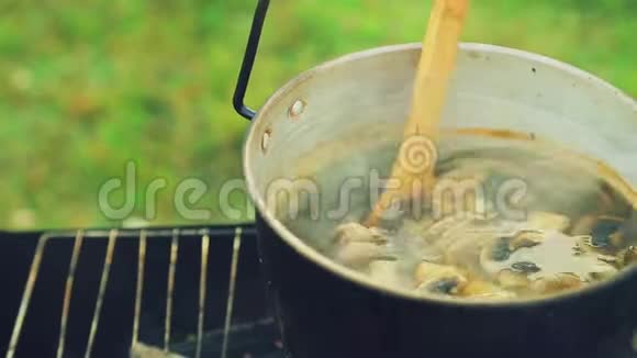 一个木勺把蘑菇搅动在锅里的火上沸腾视频的预览图