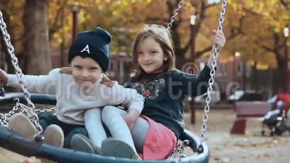 两个小孩在公园的巢上荡秋千快乐的欧洲小朋友看着镜头欢快地笑着视频的预览图