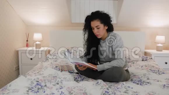 可爱的年轻漂亮的卷发黑发在床上看书视频的预览图