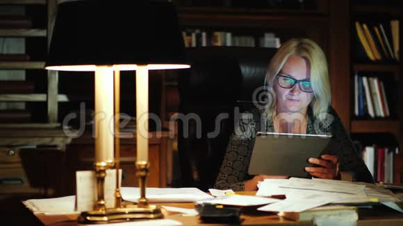 一位女老板在一间豪华办公室里用平板电脑工作背景是一个书架和一个漂亮的台灯视频的预览图