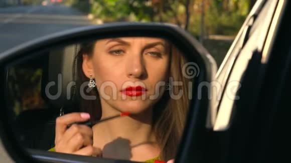 女人用红色口红涂嘴唇看着后视镜视频的预览图