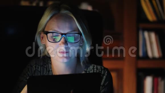 一位戴眼镜的女商人坐在一张豪华的扶手椅上背景是一个书架上放着书使用平板电脑视频的预览图
