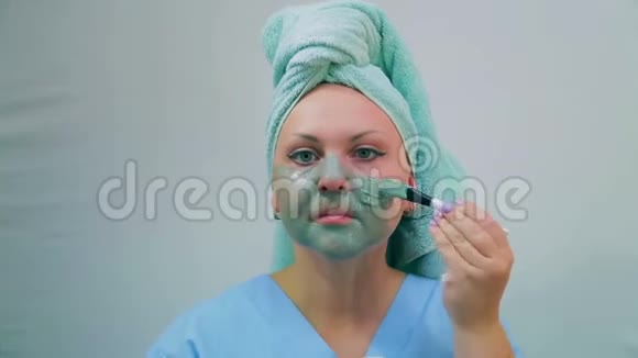 浴室里的一个年轻女子正在用刷子把一个泥面罩涂在脸上特写镜头视频的预览图