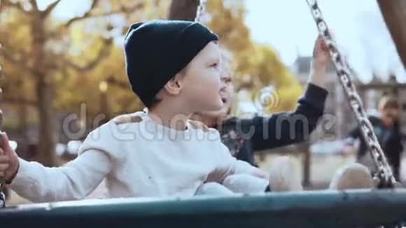 两个白人孩子在秋天公园的秋千上快乐的孩子朋友们在一个和平的阳光明媚的秋天一起摇摆视频的预览图