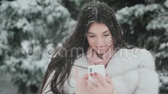白雪皑皑的冬天美丽的黑发女孩通过电话交谈的肖像视频的预览图