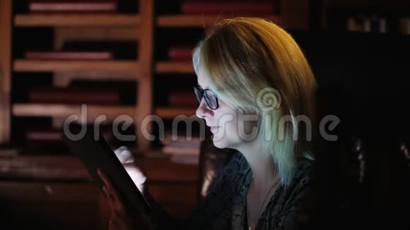 侧视图一位戴眼镜的妇女在书架背景上用一块写字板写字概念库工作或视频的预览图