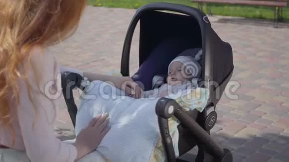 美丽的红发女人和她的孩子在公园里躺在婴儿车里玩这位女士和她一起享受阳光明媚的一天视频的预览图