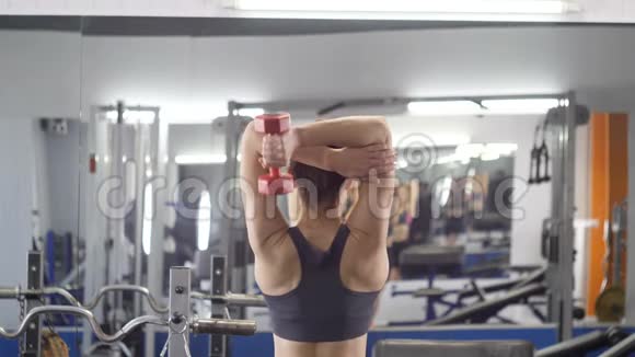 运动年轻女孩在健身房做三头肌伸展运动女人手中握着自由的重量然后低头视频的预览图