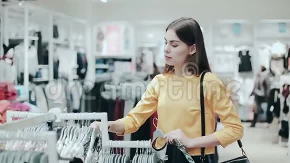 女人看着服装店里栏杆上的衣服风格和时尚理念年轻女士选择衬衫衣服视频的预览图