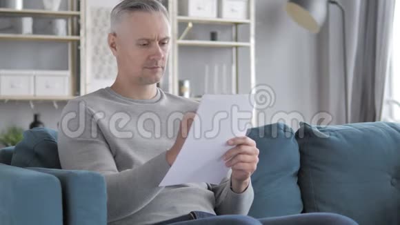 坐在沙发上做文件的白发男人视频的预览图