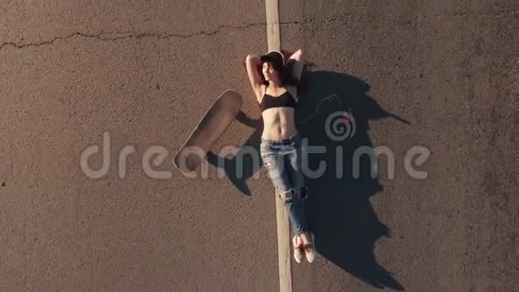 空中飞行一个穿着破烂牛仔裤和T恤的女孩躺在高速公路上带着滑板休息的女孩从上面看视频的预览图