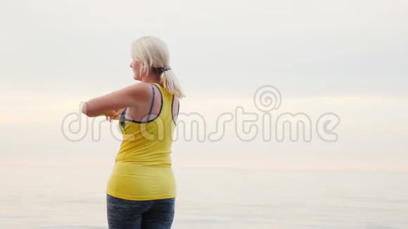一个中年妇女在海滩上温暖起来清晨视频的预览图