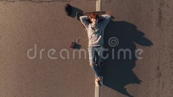 空中飞行鸟瞰一个十几岁女孩肖像一个女孩滑板者躺在马路上听音乐视频的预览图
