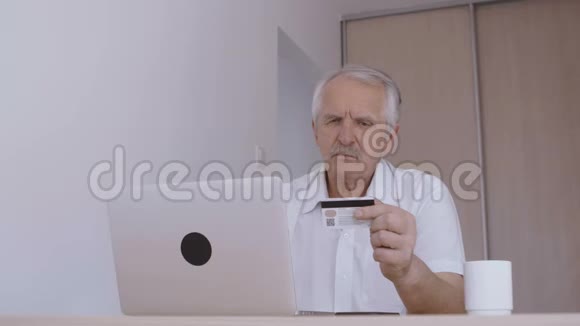 老人在家里用笔记本电脑上网打信用卡号码视频的预览图