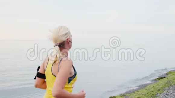 stadicam射击年轻女子在海或湖的背景下慢跑后景侧视图视频的预览图