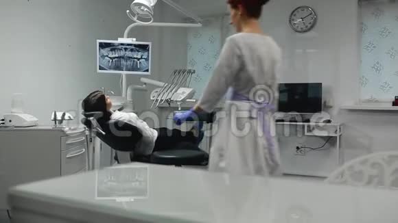 戴着蓝色手套和白色外套的女医生走近病人的椅子用X光和仪器视频的预览图
