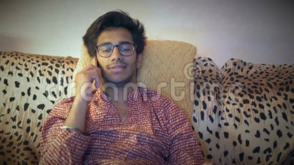 戴眼镜的印度男人在沙发上坐在家里打电话视频的预览图