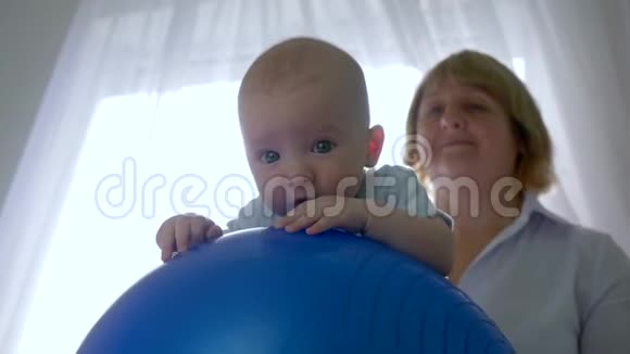 在室内专业治疗师的背景下婴儿躺在背光的充气健身球上视频的预览图