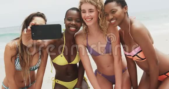 混合种族女性朋友在海滩上用手机自拍的正面景色视频的预览图