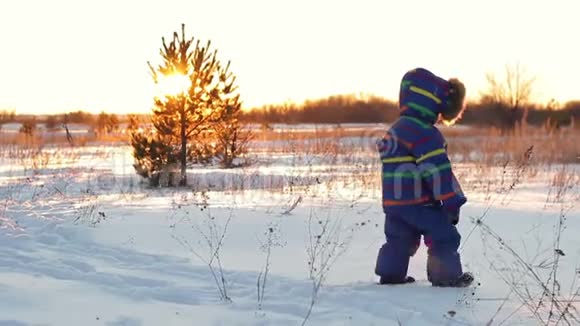 这个小男孩在日落的背景下在冬天穿过雪堆视频的预览图