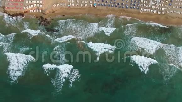 头顶的鸟瞰在蔚蓝的沙滩上飞翔人们在毛巾上晒日光浴在绿水中玩耍视频的预览图
