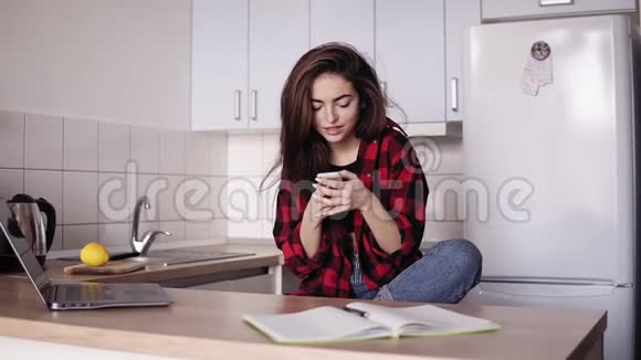 漂亮的黑发女孩坐在她公寓的厨房里发短信给别人视频的预览图