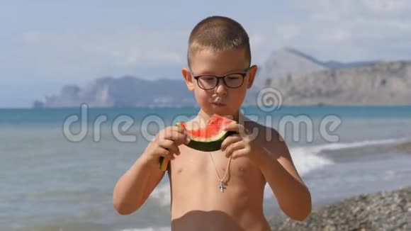 孩子们在海滩上玩在沙子里吃西瓜的男孩孩子手里拿着一块绿色的瓜皮视频的预览图