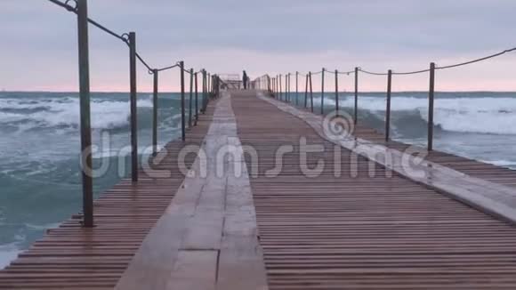 一家人正在暴风雨中走在海港波浪在海上的木墩上飞溅美丽的海景视频的预览图