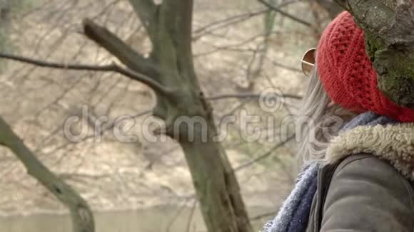 年轻漂亮的女人戴着红帽子坐在公园的树旁环顾四周视频的预览图