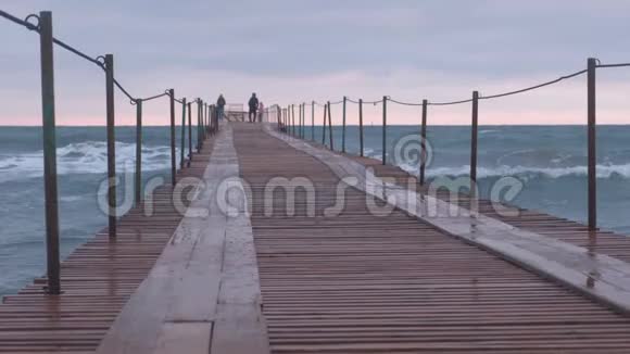 一家人正在暴风雨中走在海港波浪在海上的木墩上飞溅美丽的海景视频的预览图