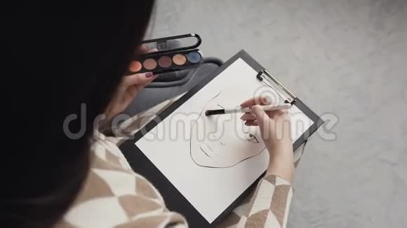 上景年轻的女化妆师在明亮的工作室画一张脸图化妆师绘制了一幅视频的预览图
